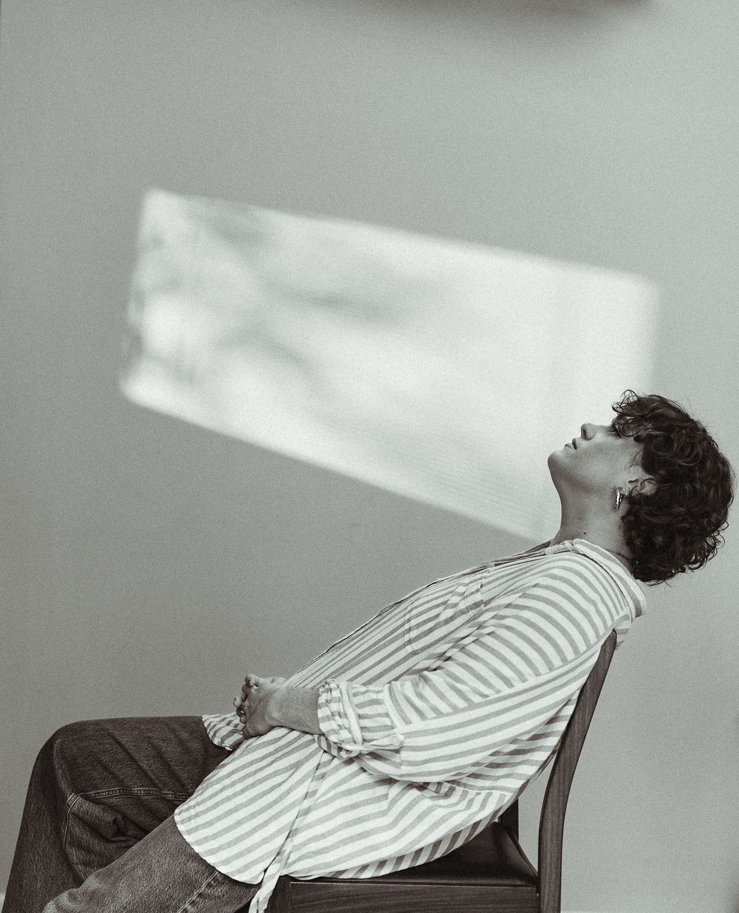 Person sitting in chair with head tilted back, wearing striped shirt, black and white portrait photography.