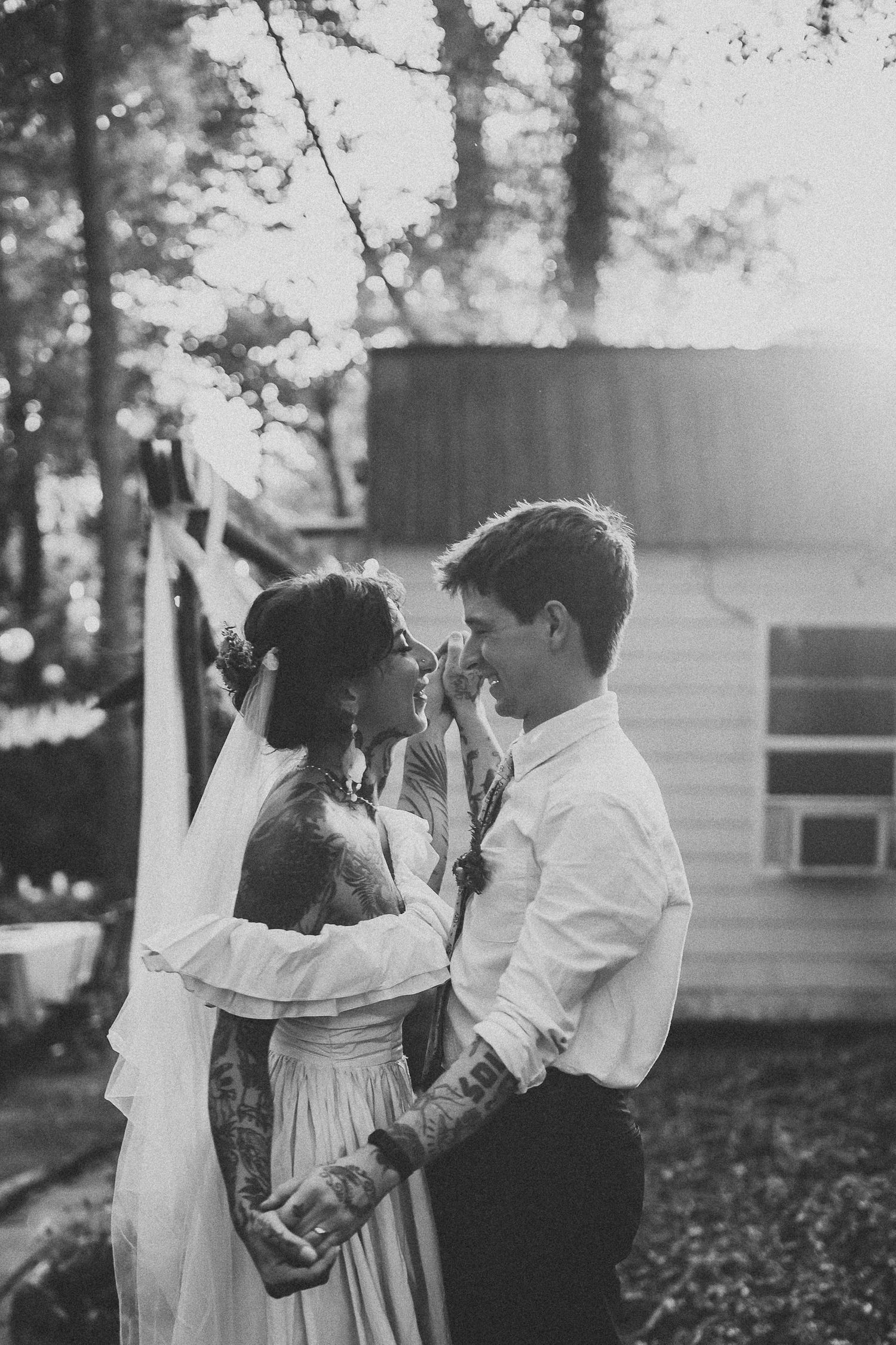 Black and white portrait of tattooed bride and groom sharing an intimate moment outdoors.