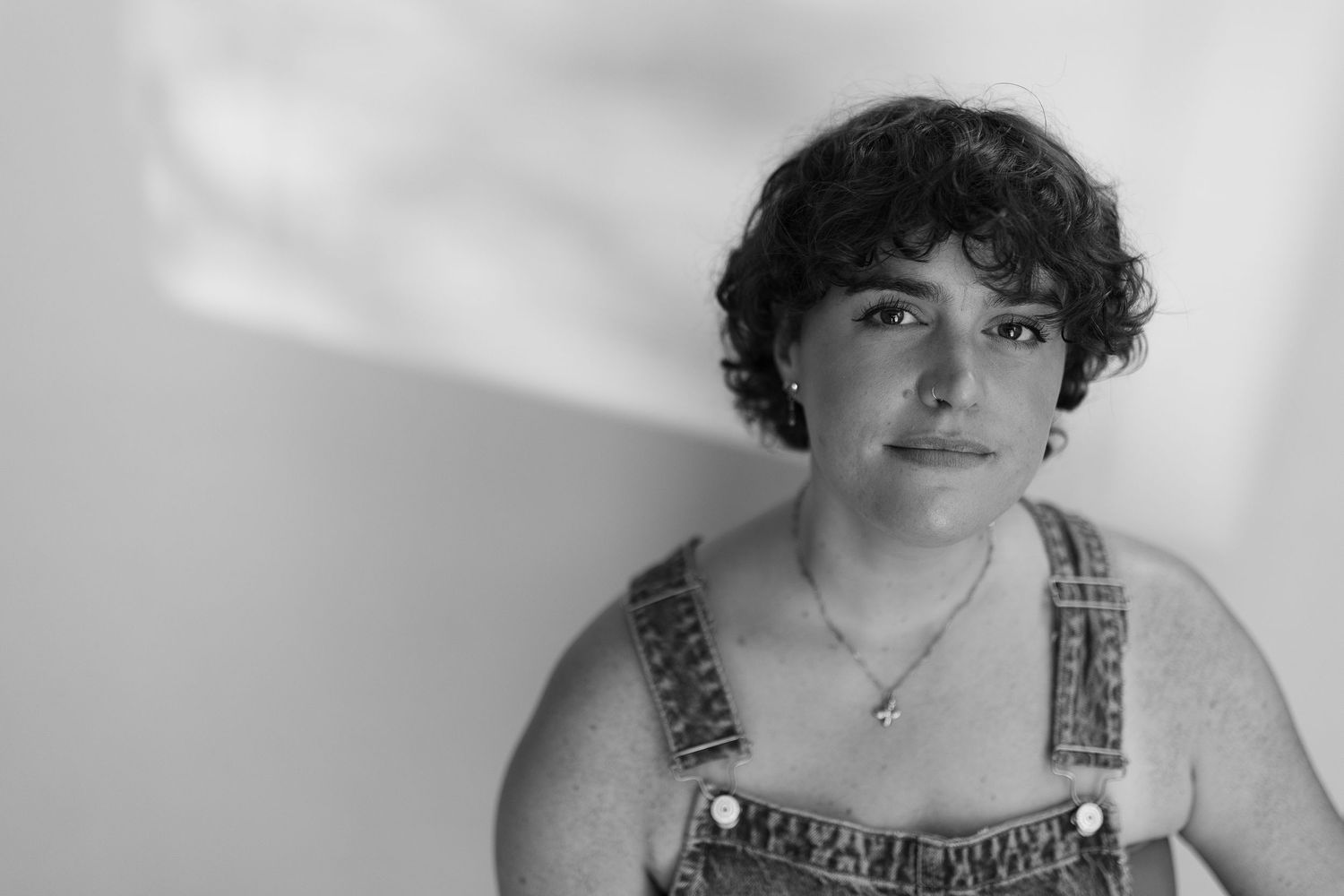 Black and white portrait of a young person with curly hair wearing denim overalls.