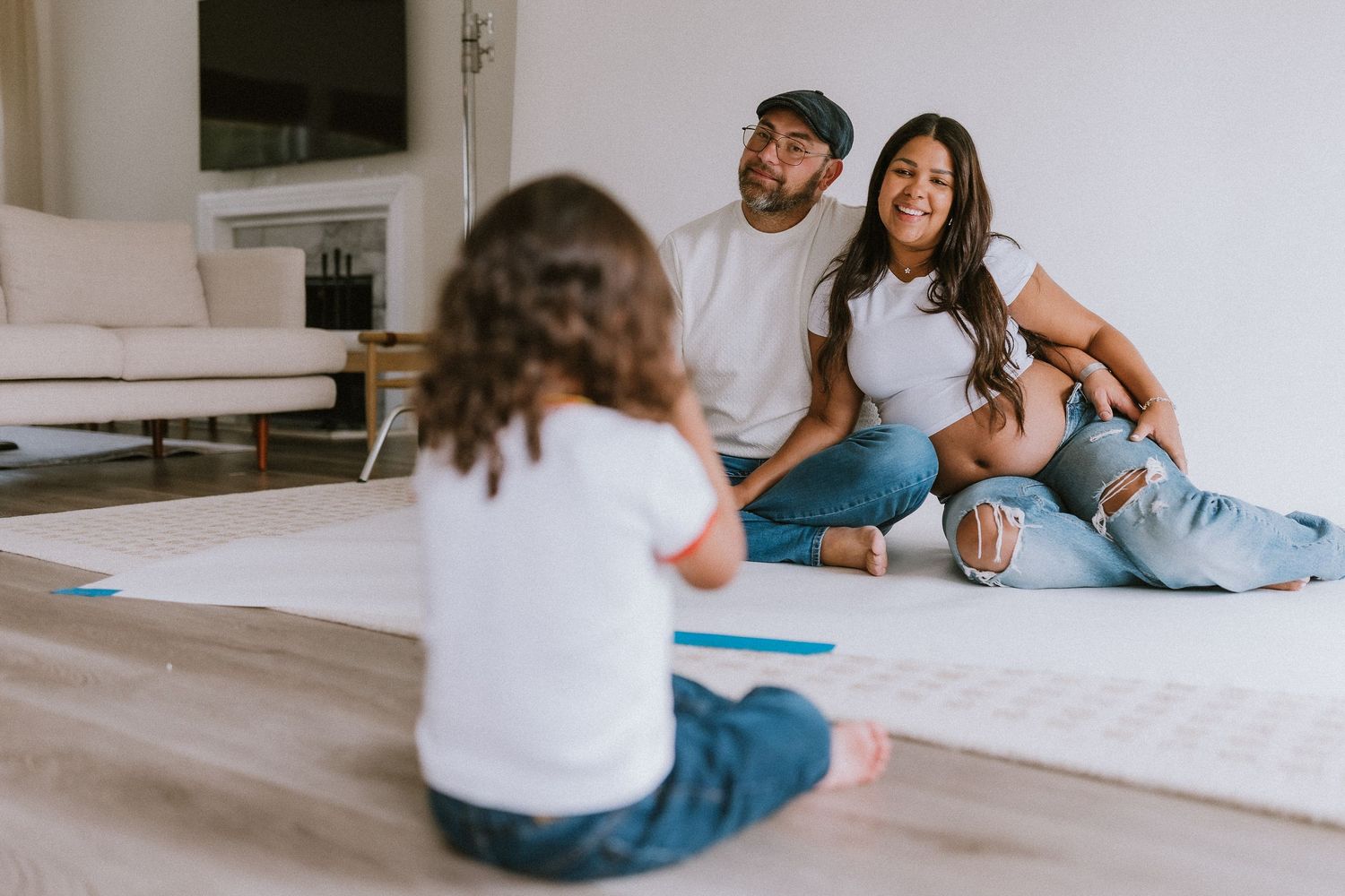 Family sitting on living room floor together, parents smiling at young child during a relaxed home moment.