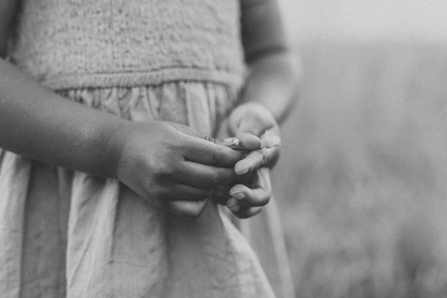 Black and white photo of a young girl in a dress holding hands together in a field.