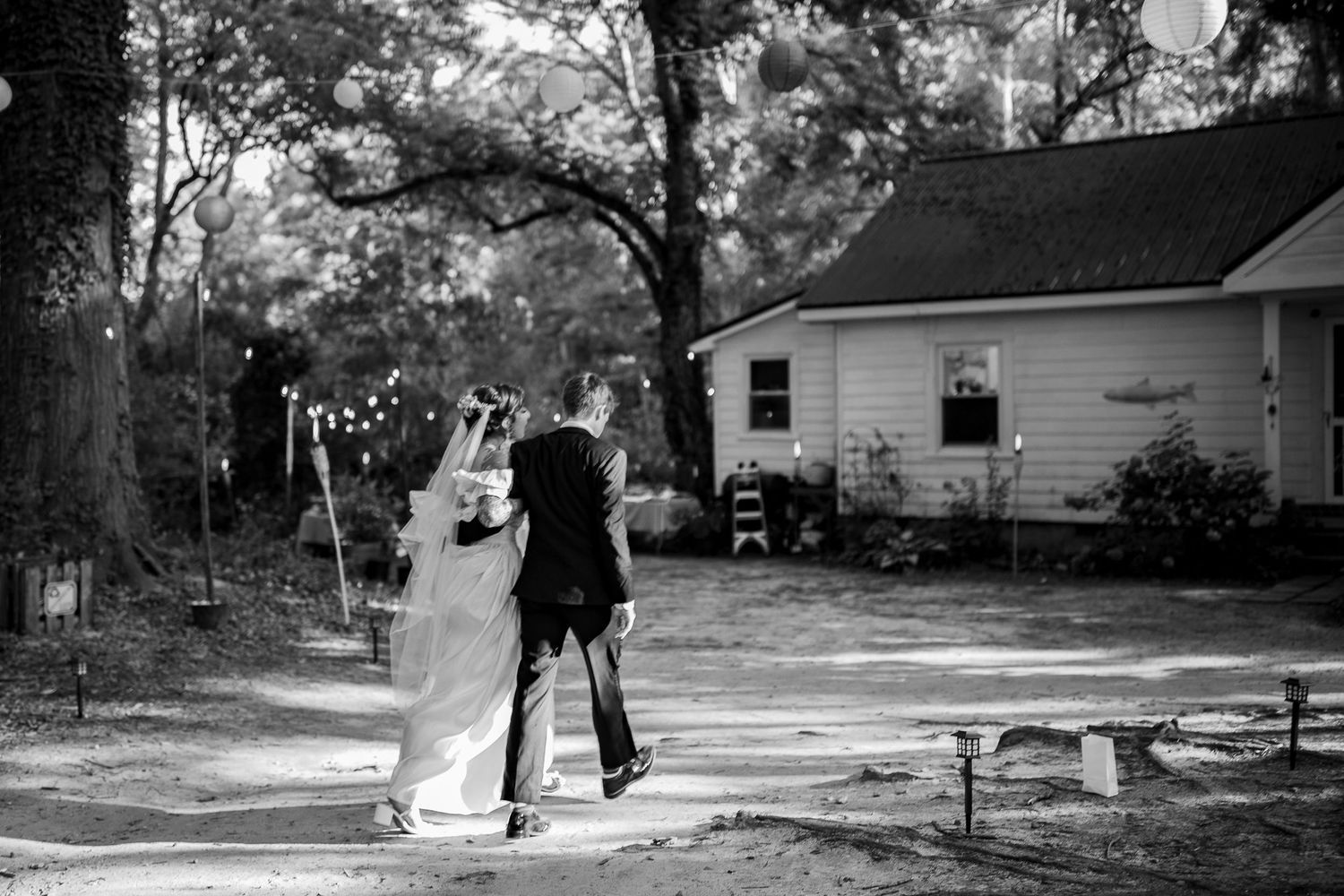 Black and white photo of a bride and groom walking together along a path at an outdoor wedding venue.
