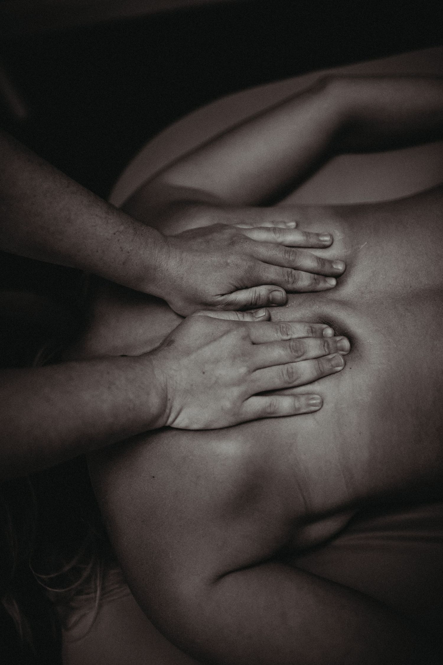 Close-up black and white photo of hands providing back massage on bare skin.