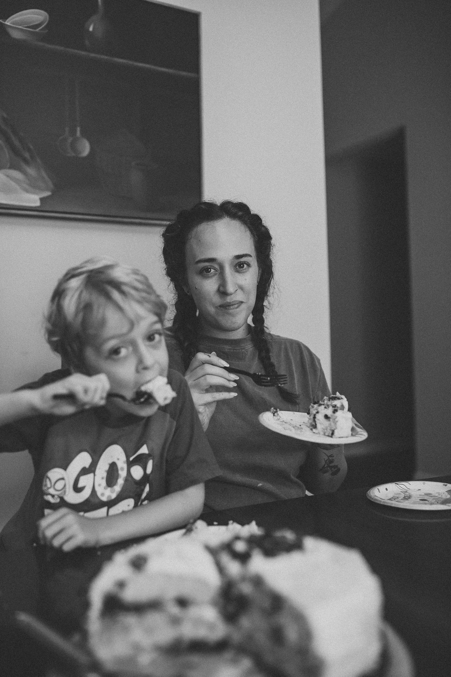 Black and white photo of woman and child eating birthday cake together indoors.