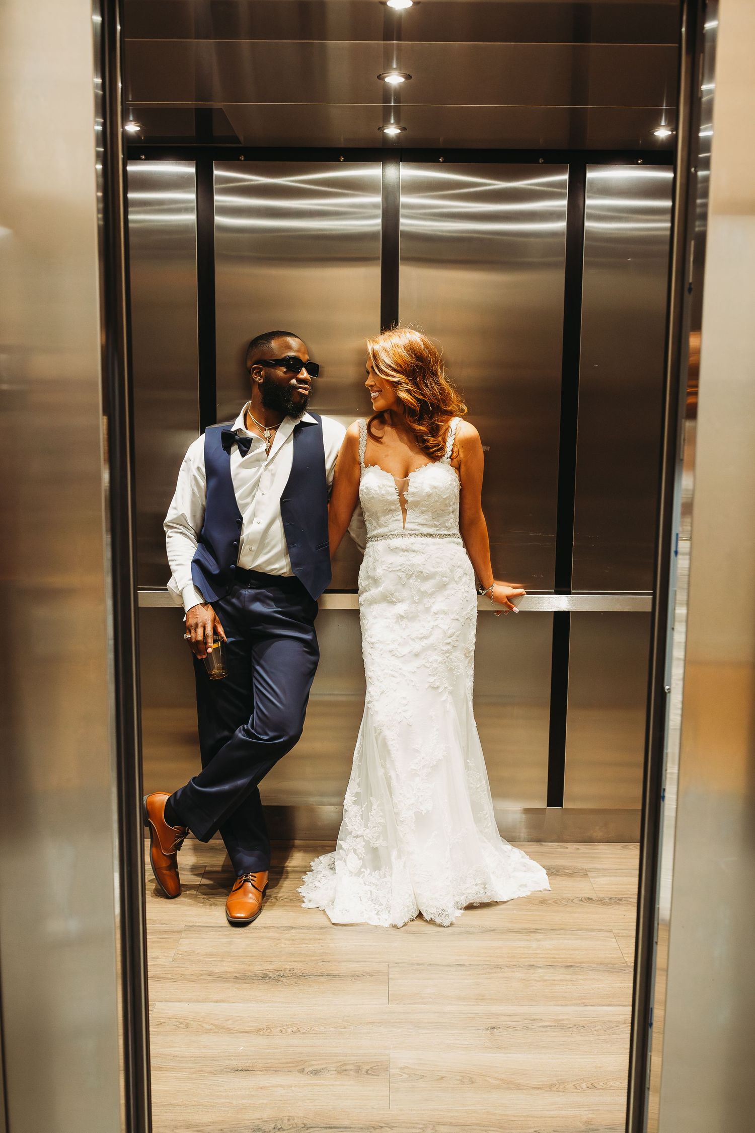 Elegant bride and groom posing together in a modern mirrored elevator on their wedding day.