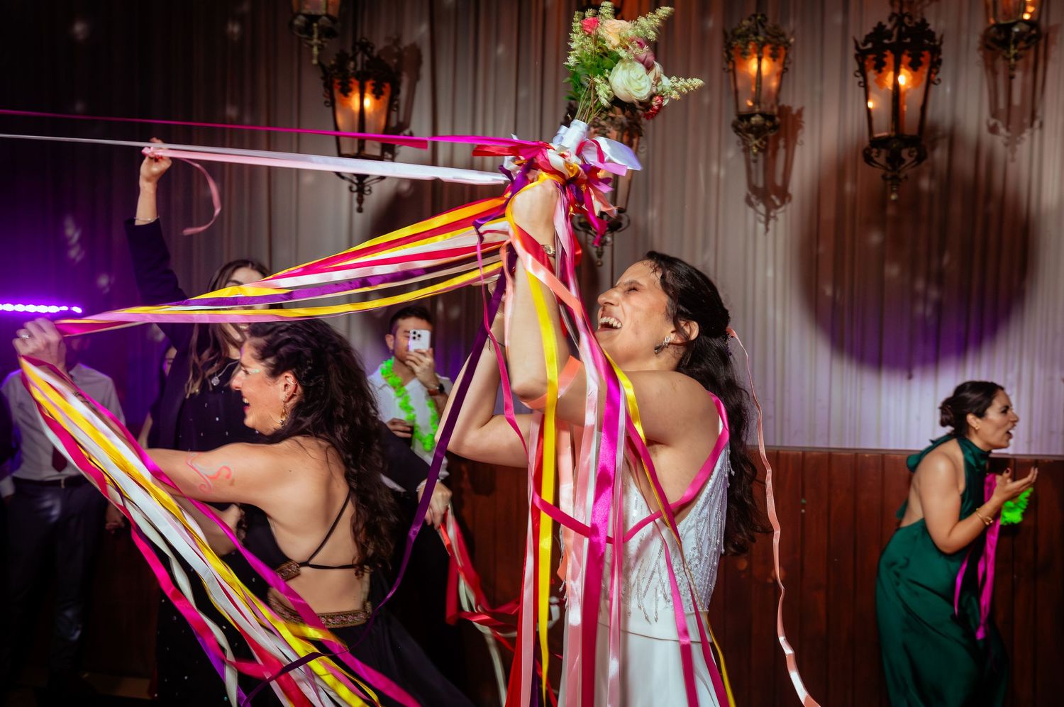 Bride and guests celebrate with vibrant colorful ribbons on wedding reception dance floor.