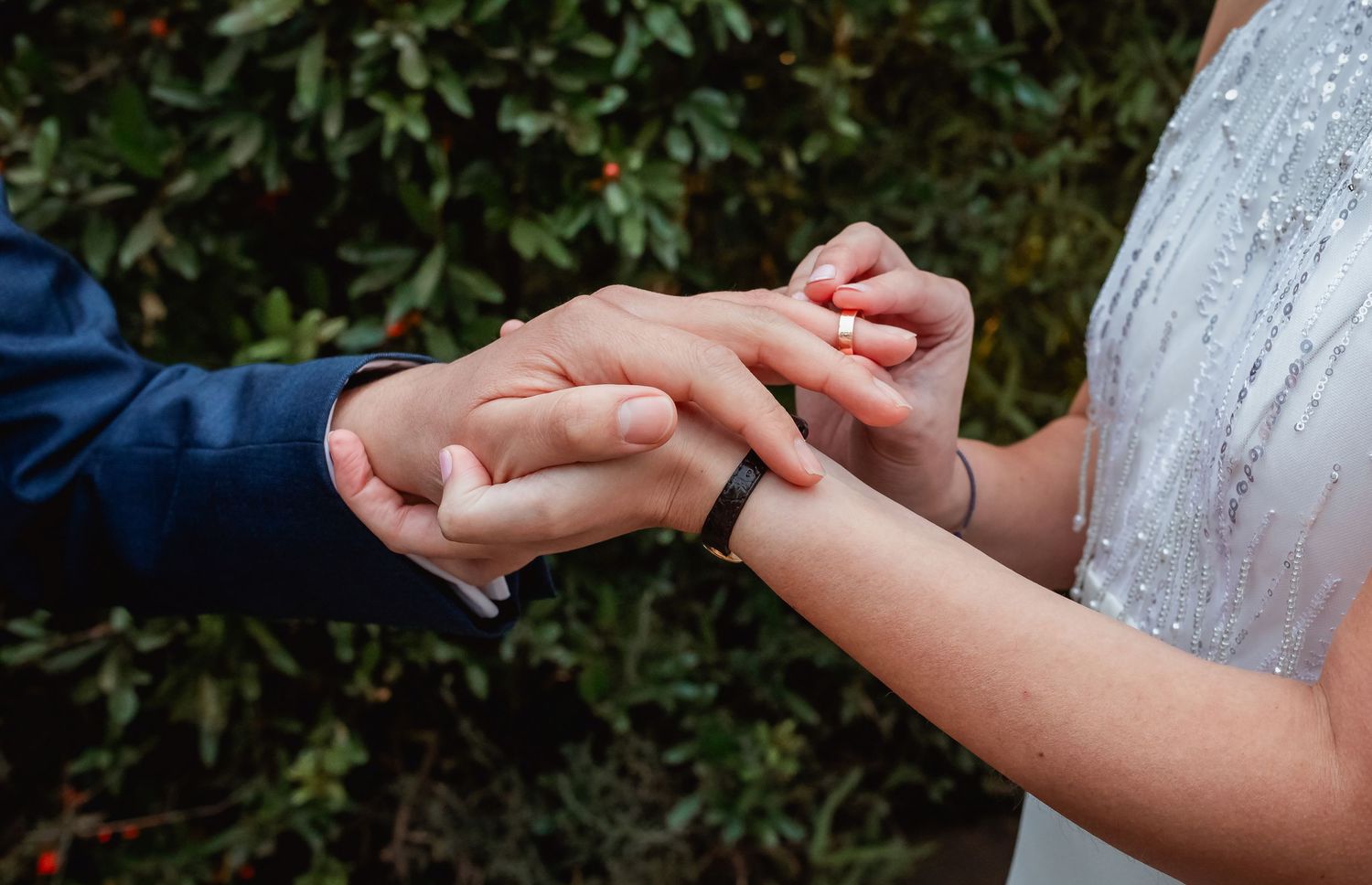 Couple exchanging wedding rings outdoors with green foliage background.