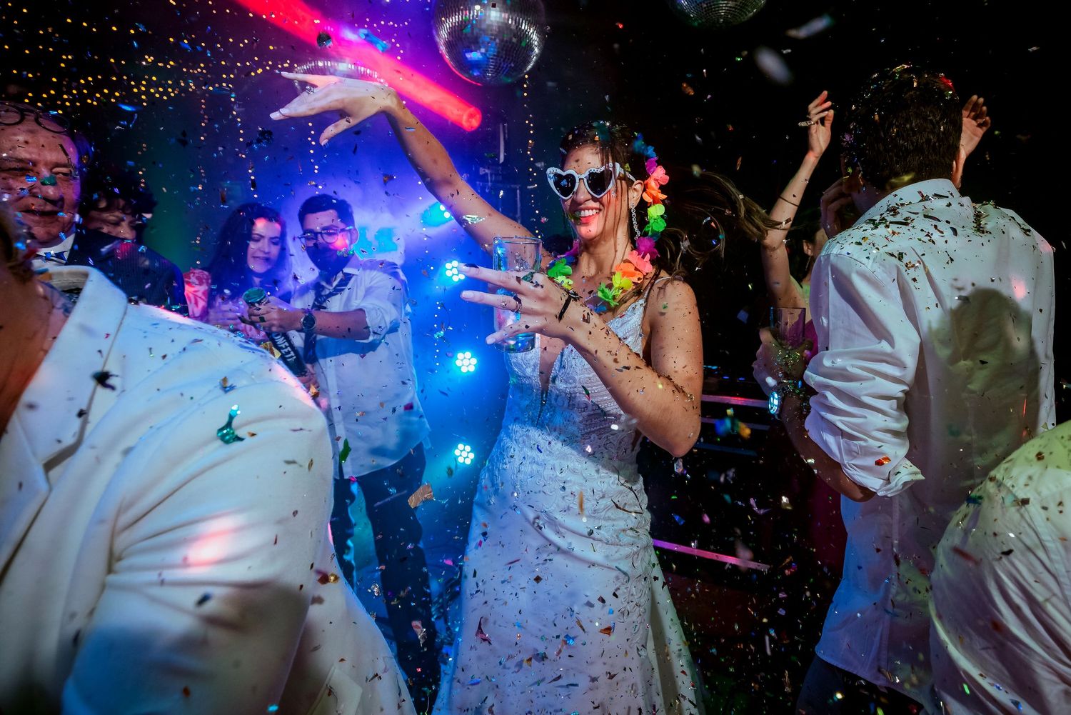 Bride in white dress with LED lights dances joyfully at wedding reception with confetti falling.