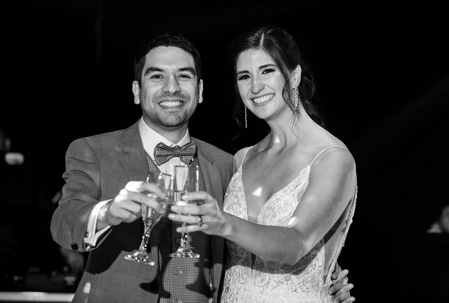 Black and white photo of smiling bride and groom toasting with champagne glasses at their wedding reception.