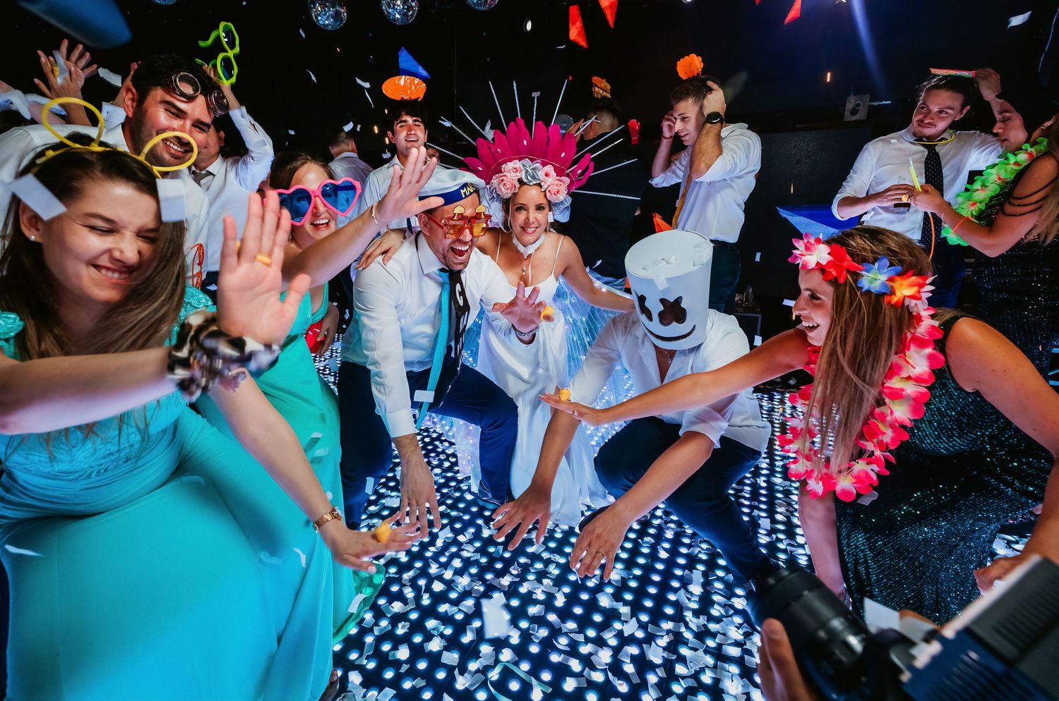 Joyful wedding guests dancing and celebrating with colorful accessories and confetti on a disco dance floor.