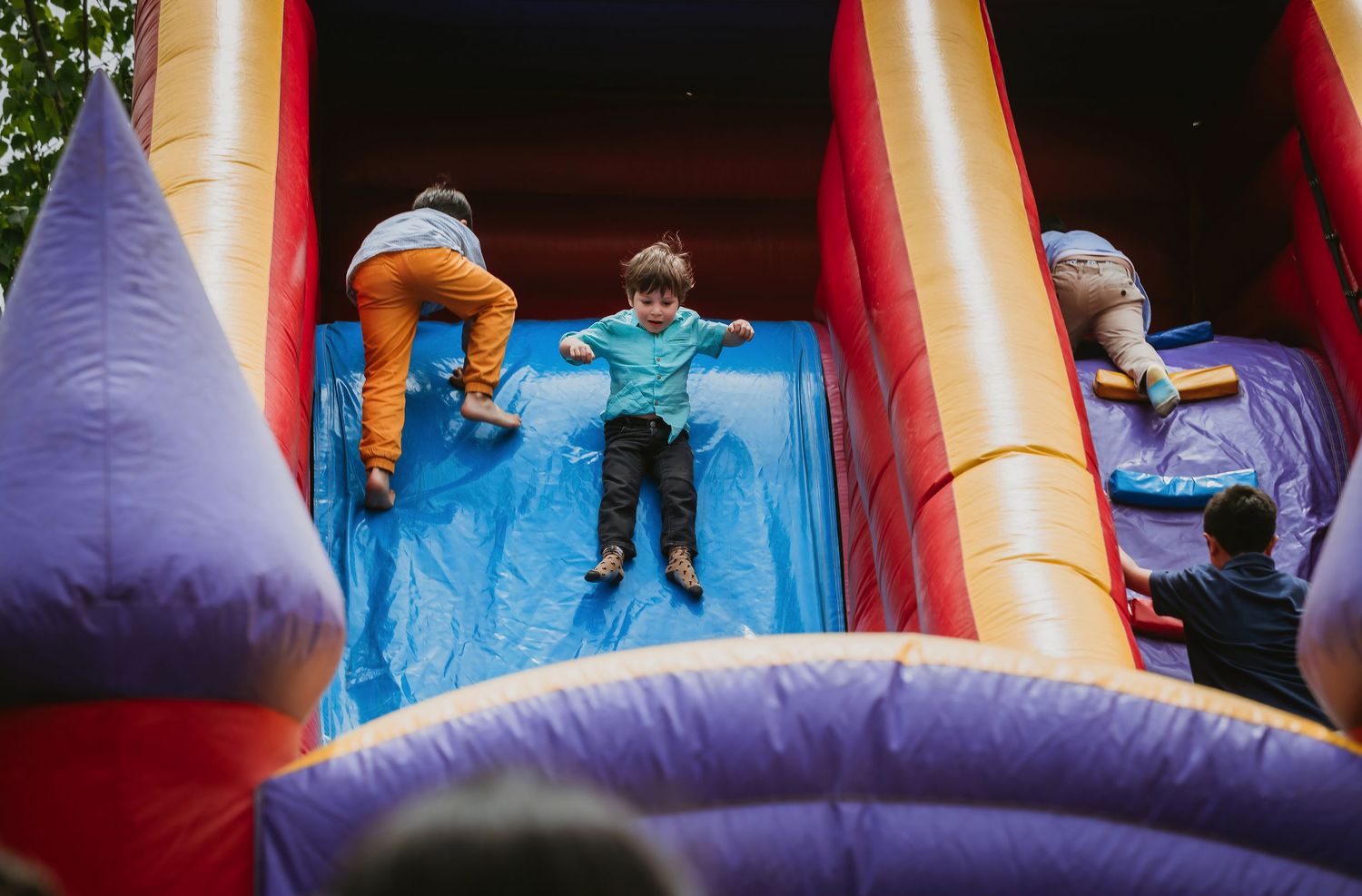 Children playing on a colorful inflatable bounce house slide at an outdoor party event.