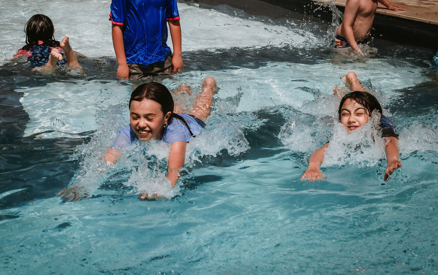 Children splashing and playing joyfully in a outdoor swimming pool on a sunny day.