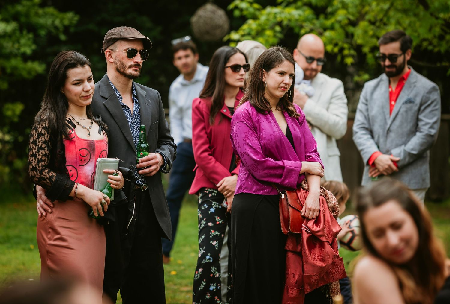 Guests in colorful attire gather outdoors at a garden party or wedding reception on a sunny day.