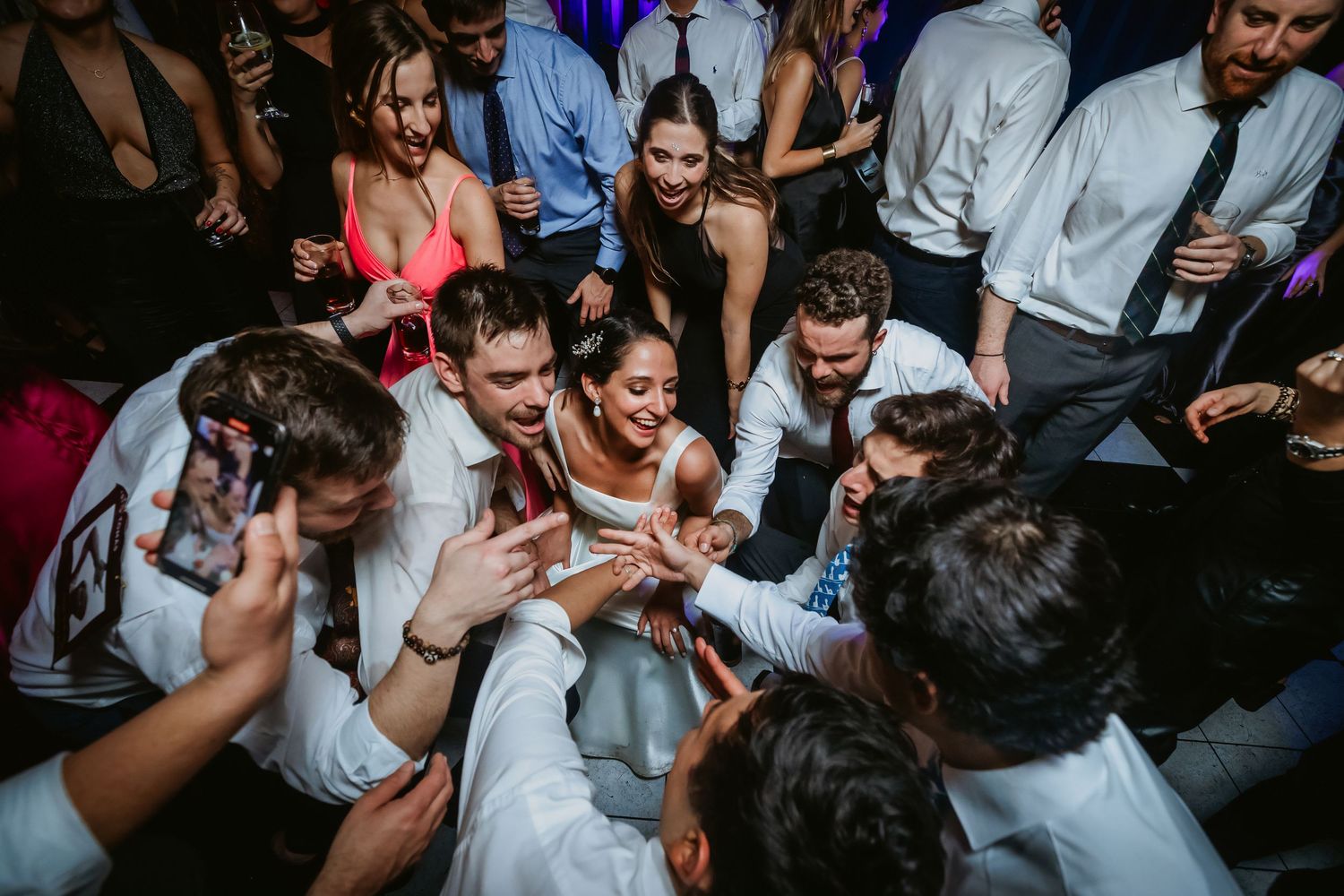 Bride and groom surrounded by guests on a lively wedding reception dance floor celebration.