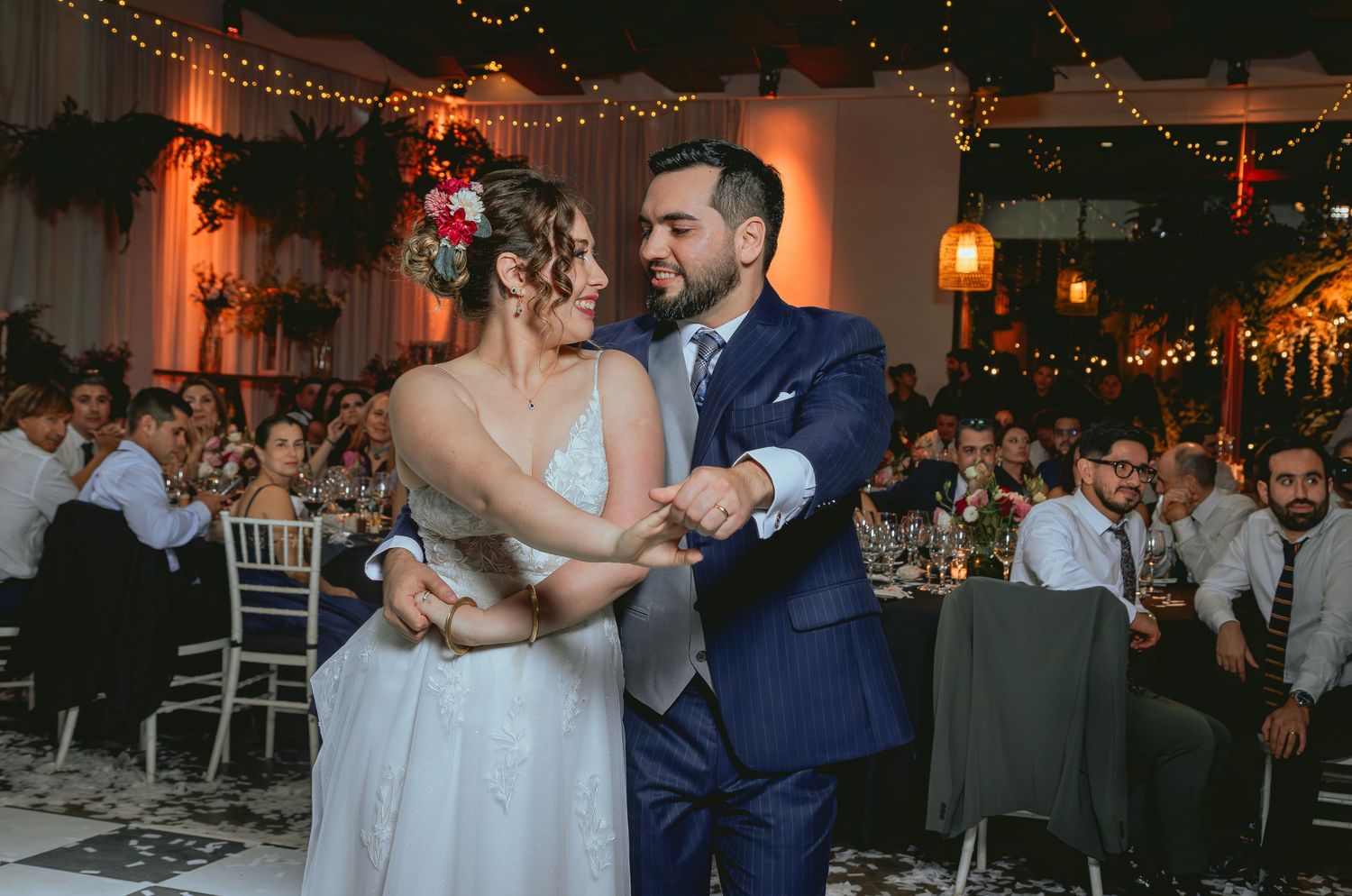 Bride and groom dance together at romantic wedding reception decorated with string lights and lush greenery.