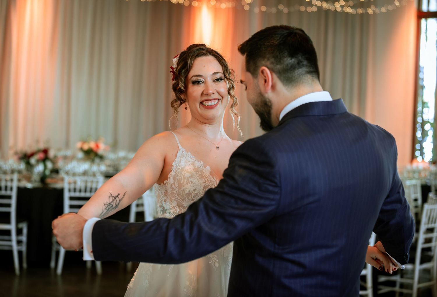 Bride and groom share a joyful first dance in an elegantly decorated wedding reception hall.