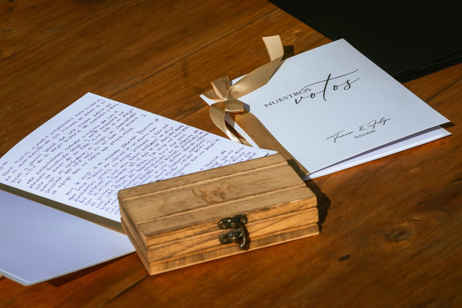 Wedding vow booklets with handwritten notes beside a rustic wooden box on a wooden table.
