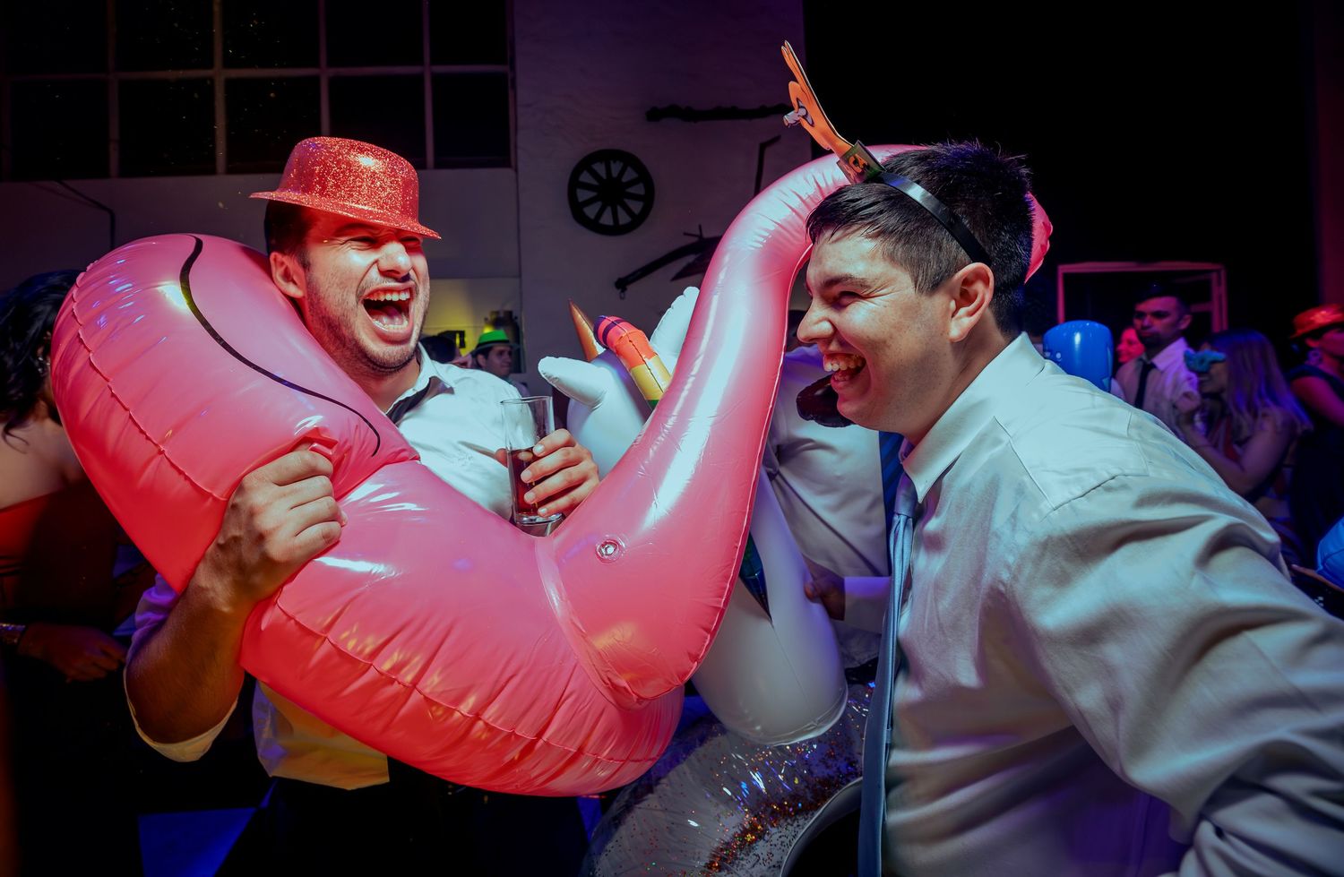 Two men laughing with pink flamingo inflatable float at wedding reception.