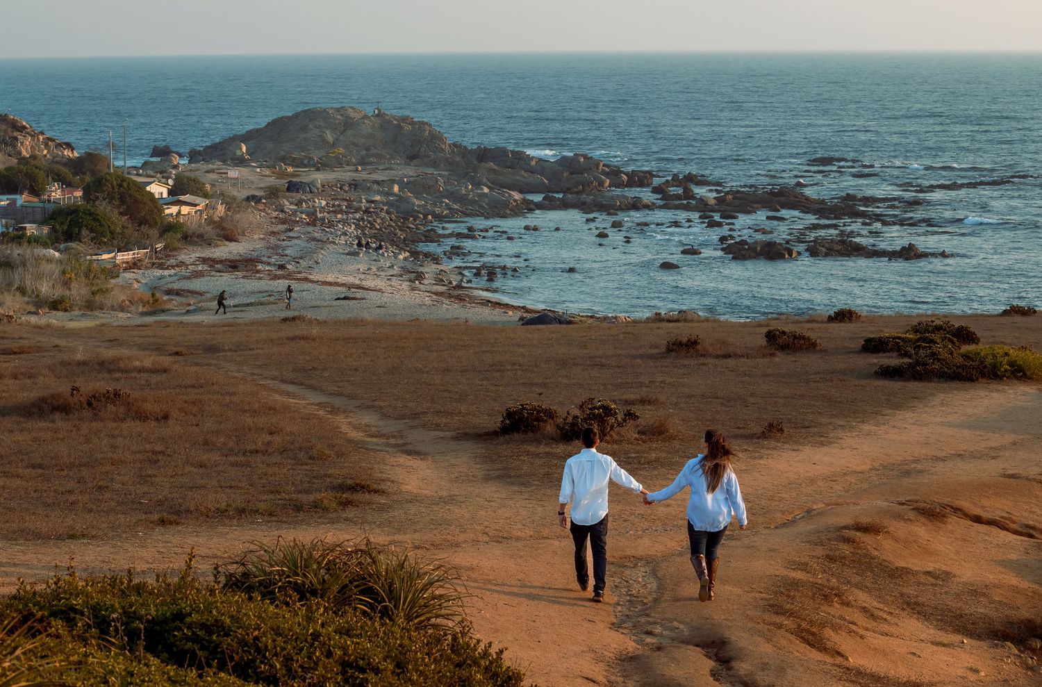 Couple holding hands walking down a coastal trail with ocean views.