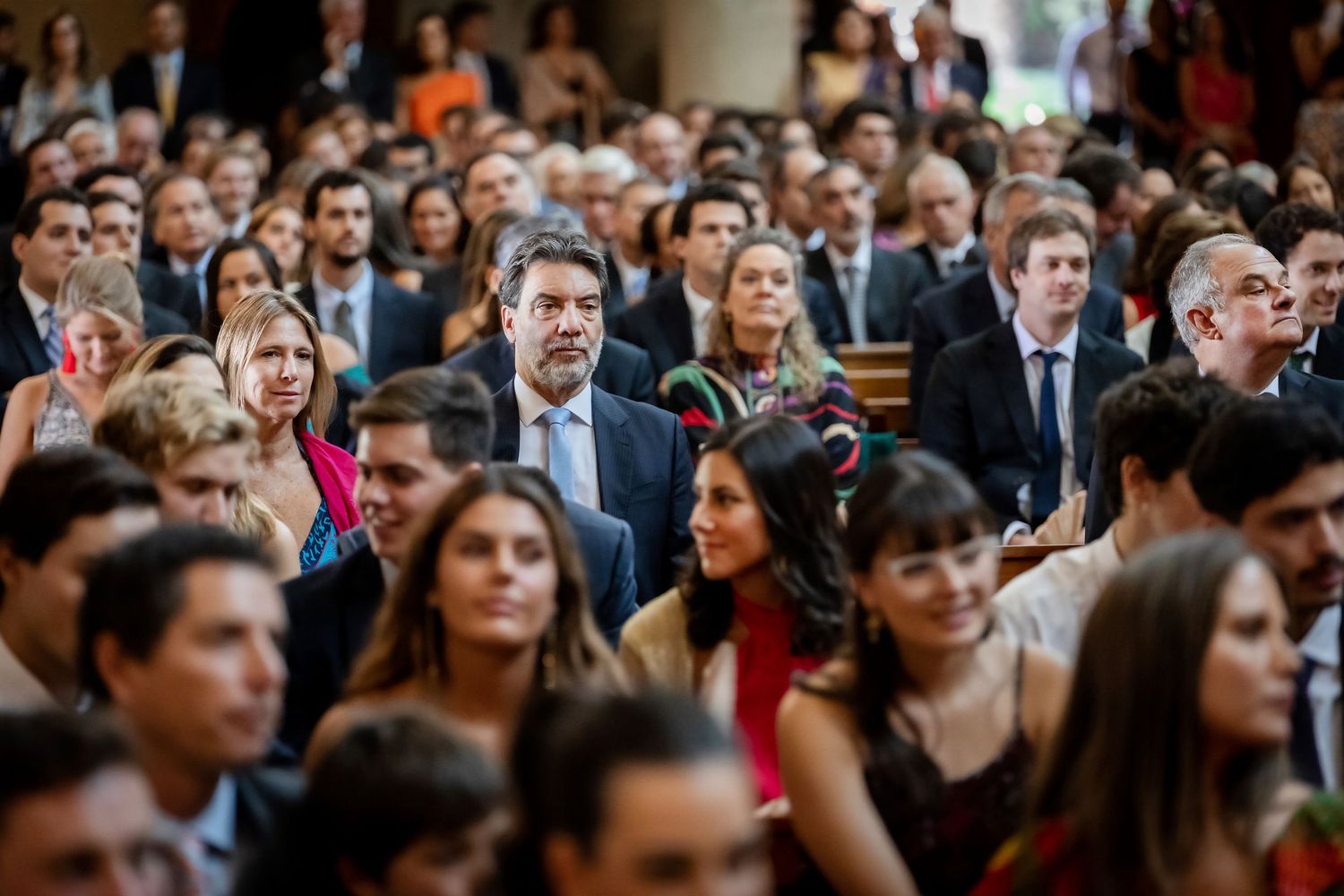 Large crowd of elegantly dressed wedding guests seated in a beautifully decorated church.