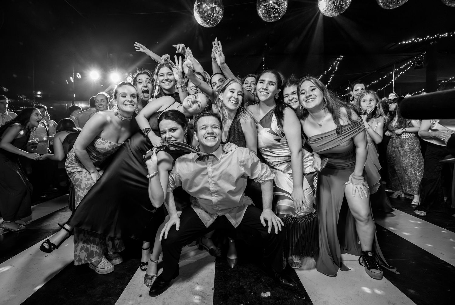 Black and white photo of groom posing with smiling wedding guests on dance floor.