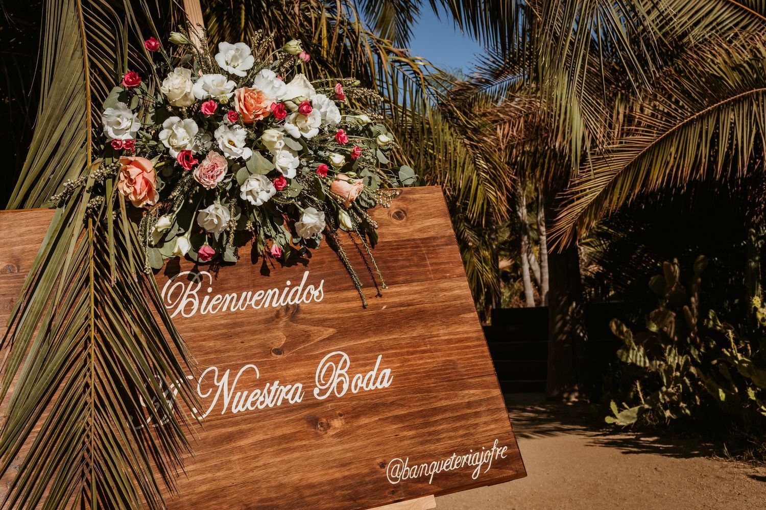 Wooden welcome sign reading Bienvenidos a Nuestra Boda decorated with flowers at outdoor wedding.