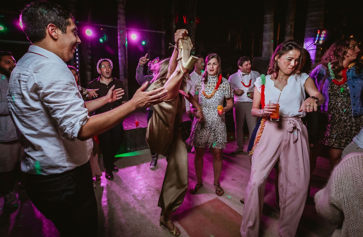 Guests dancing together under purple lights at a festive indoor wedding reception.