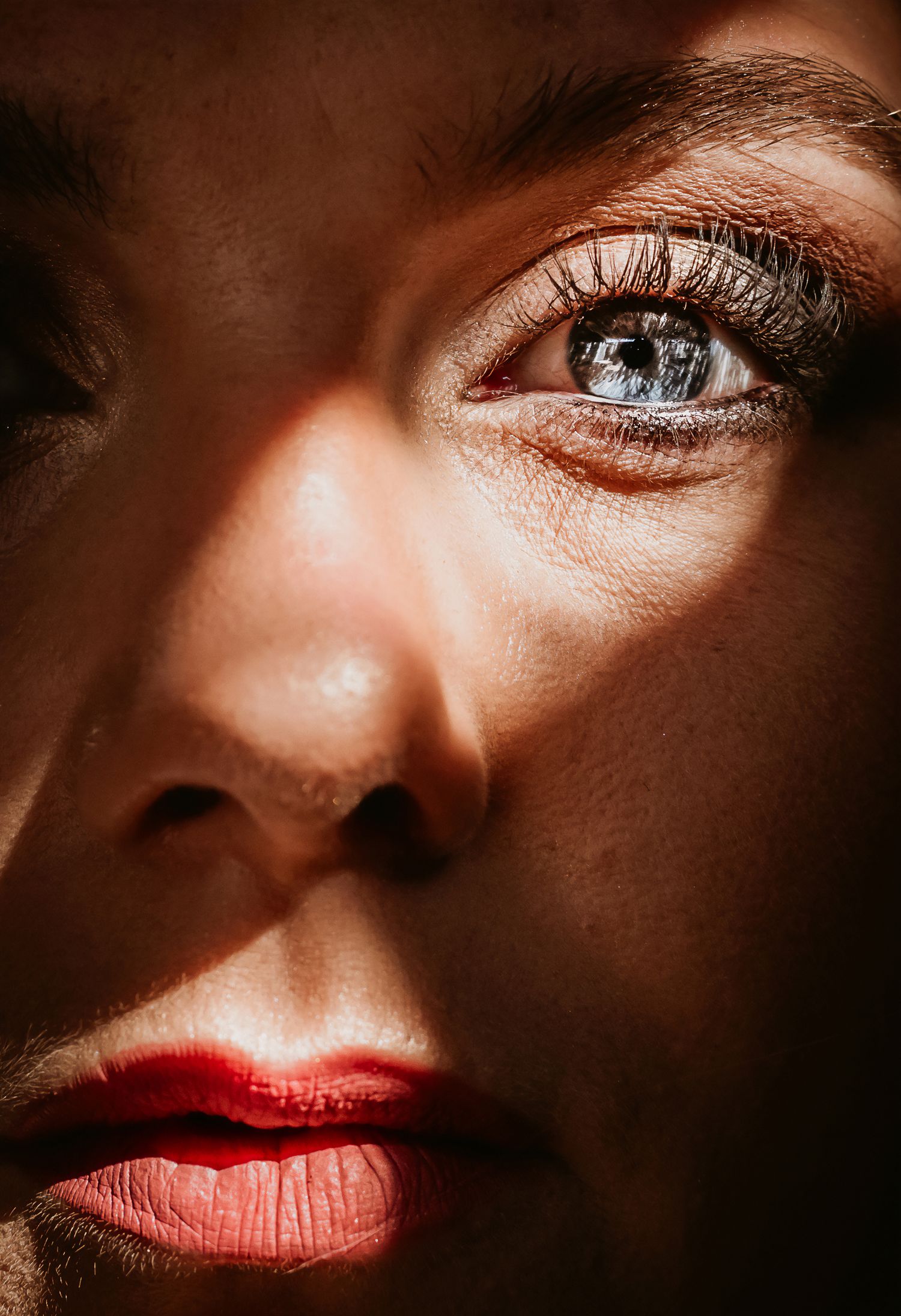 Close-up portrait of a woman with blue eyes and red lips, dramatically lit with contrasting light and shadow.