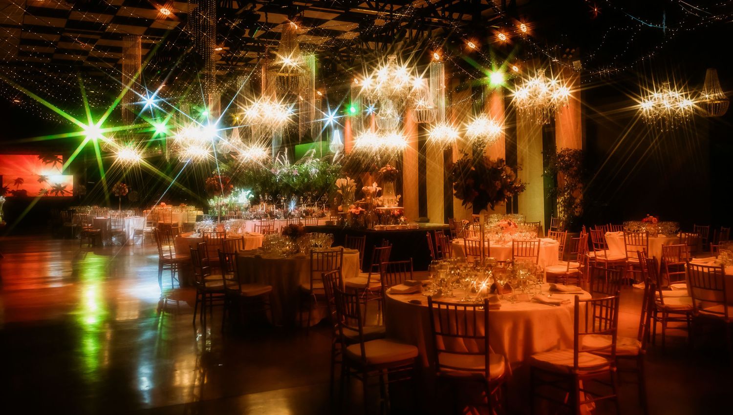 Grand wedding reception venue with colorful star-burst lights, round tables, and golden chiavari chairs.