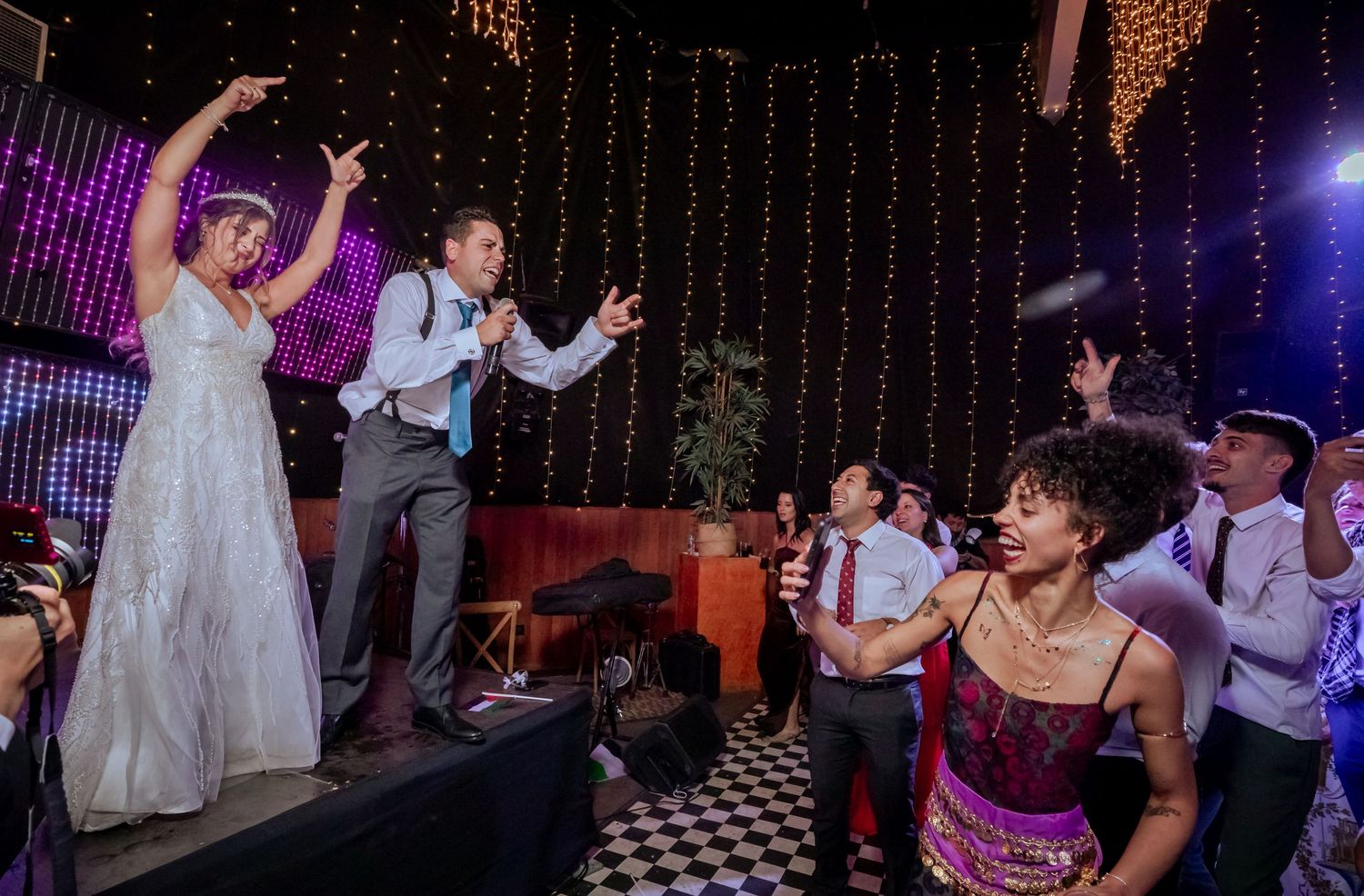 Bride and groom singing on stage with guests dancing and celebrating at their wedding reception.