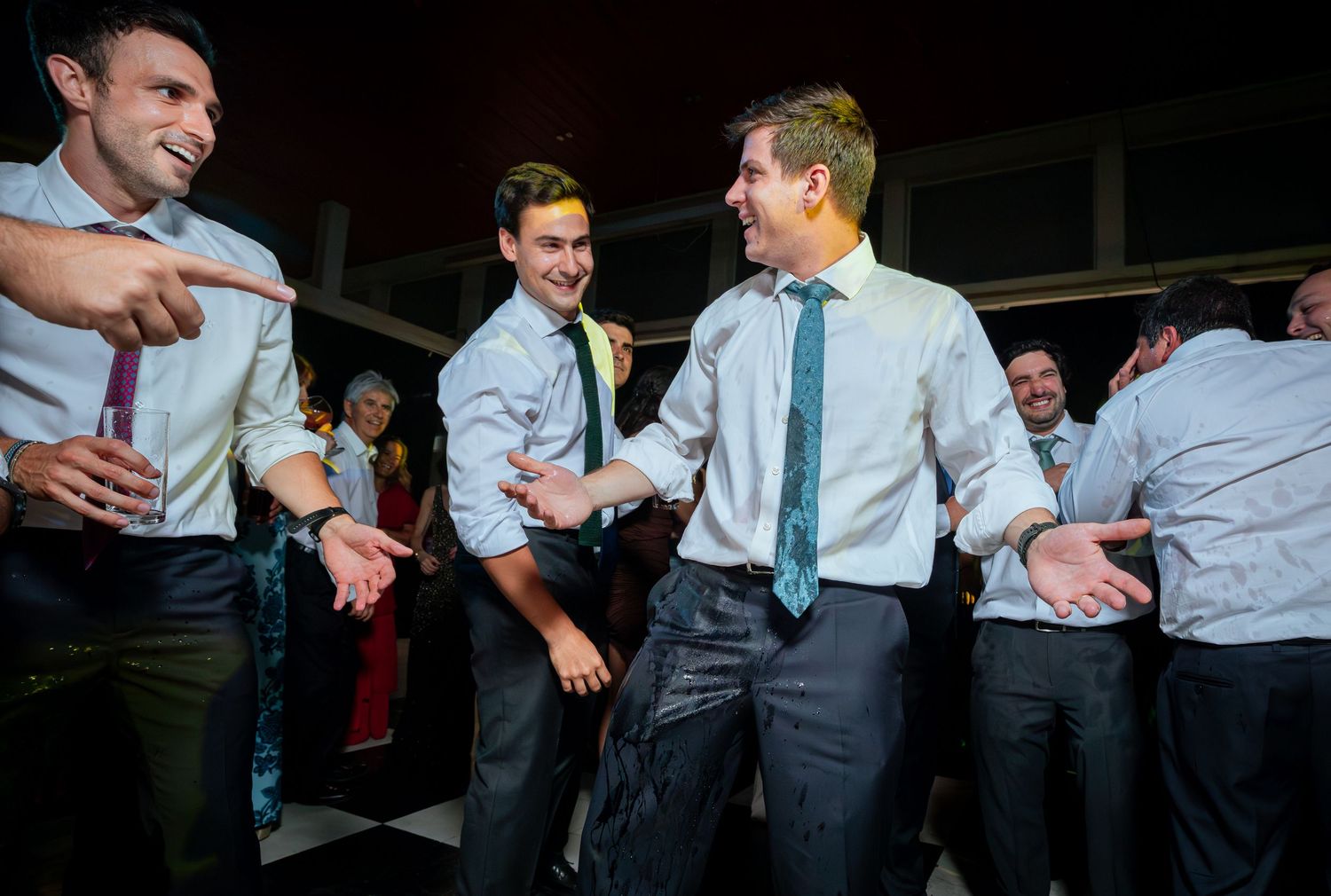 Male wedding guests dancing and laughing together on a checkered dance floor during a wedding reception.
