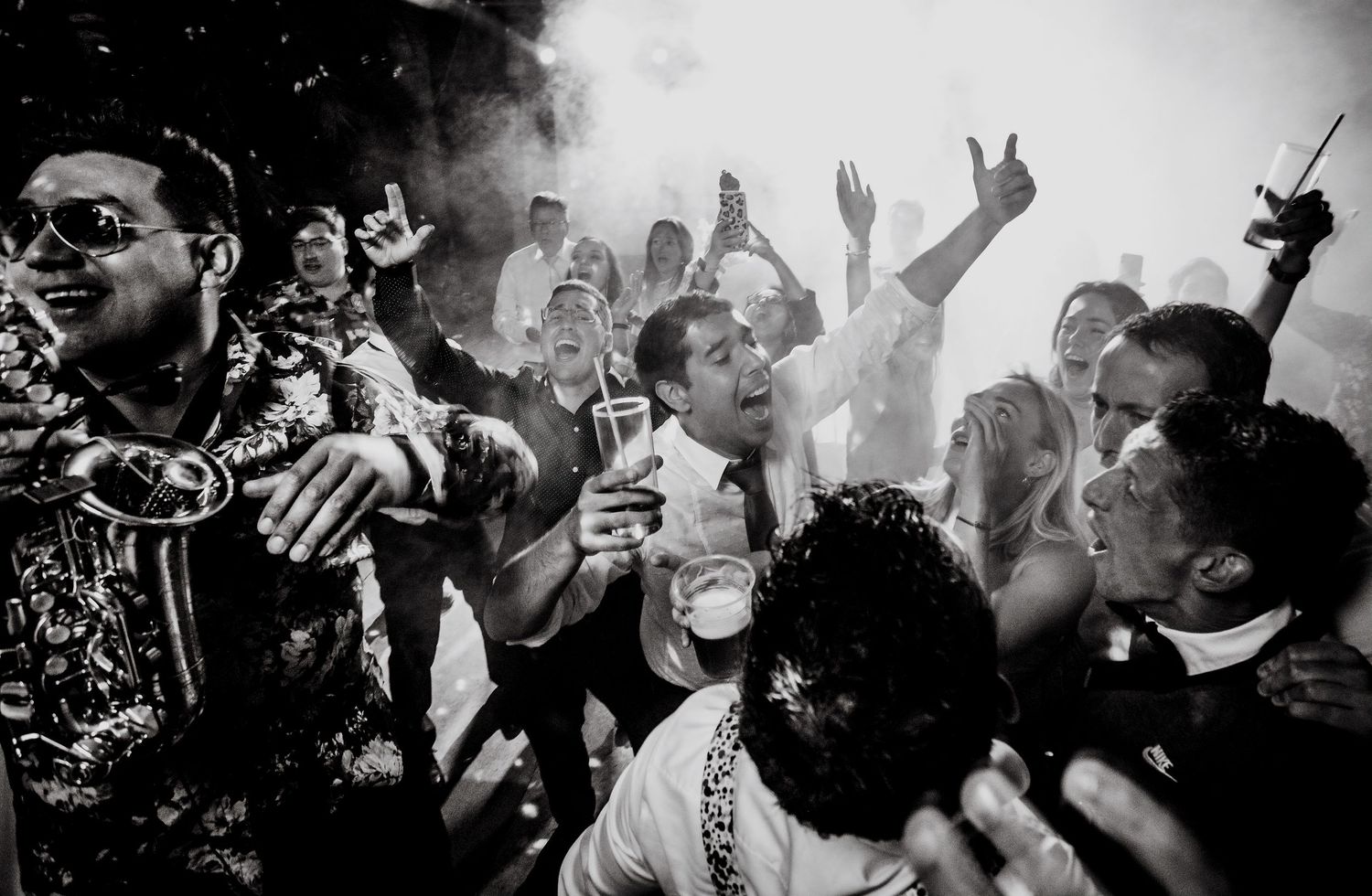 Black and white photo of lively wedding reception crowd celebrating with drinks.