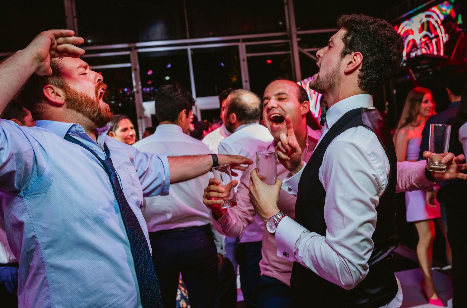 Two men laughing and celebrating together at a lively wedding reception party.