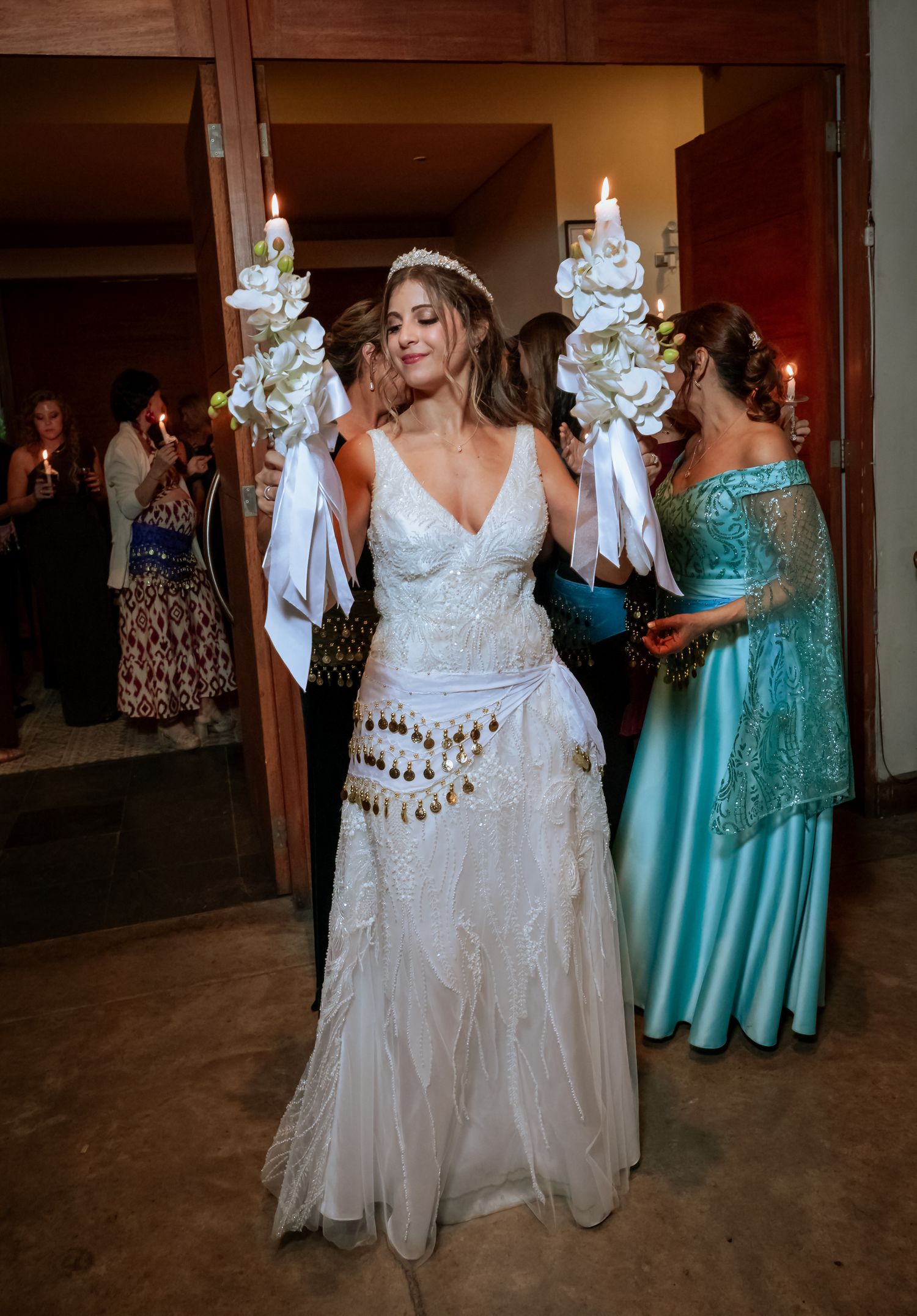 Bride in white gown holding floral candles during a traditional wedding entrance ceremony.