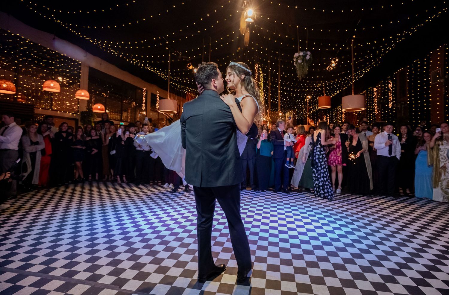 Couple shares a romantic kiss during their first dance on a black and white checkered dance floor.