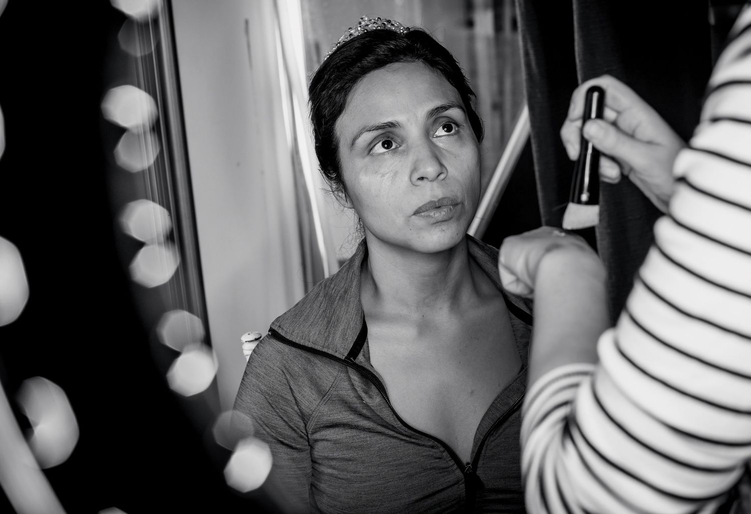 Black and white photo of a woman getting makeup applied in a dressing room.