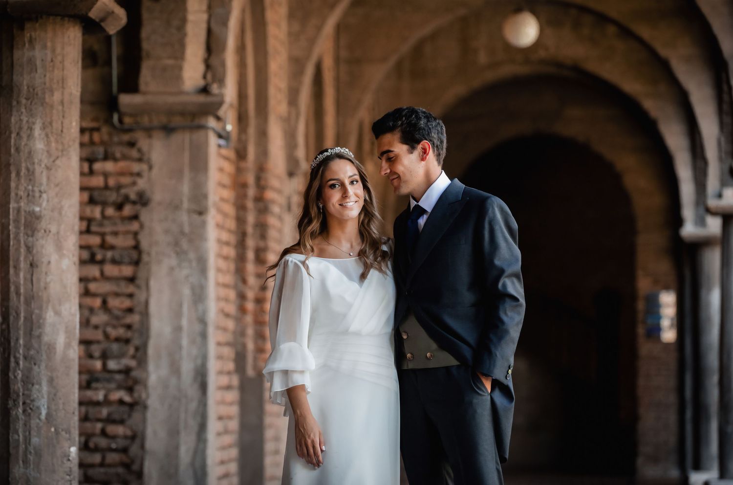 Bride and groom sharing a tender moment under elegant stone arched colonnade.