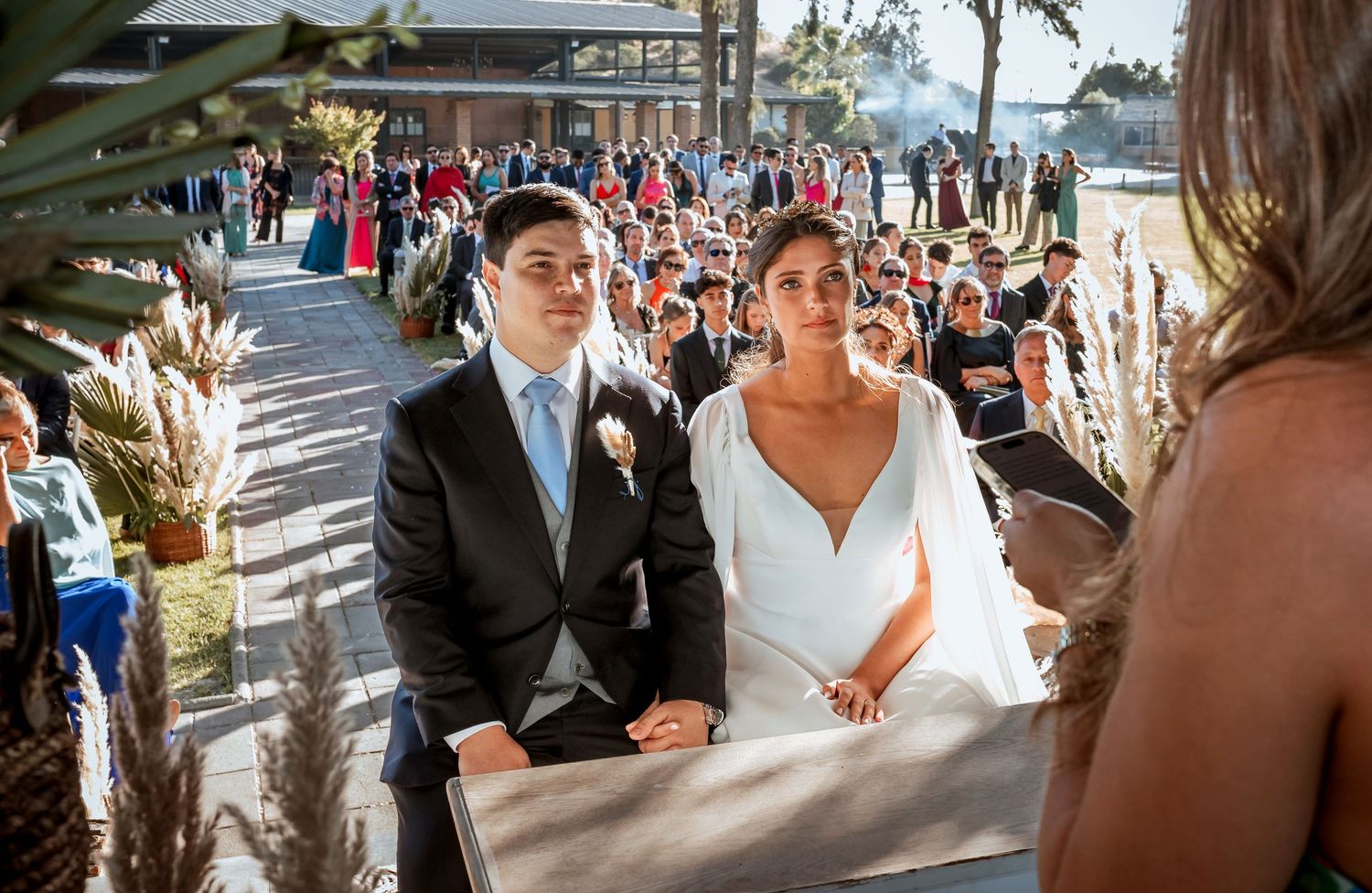Bride and groom standing at outdoor wedding ceremony altar surrounded by guests.