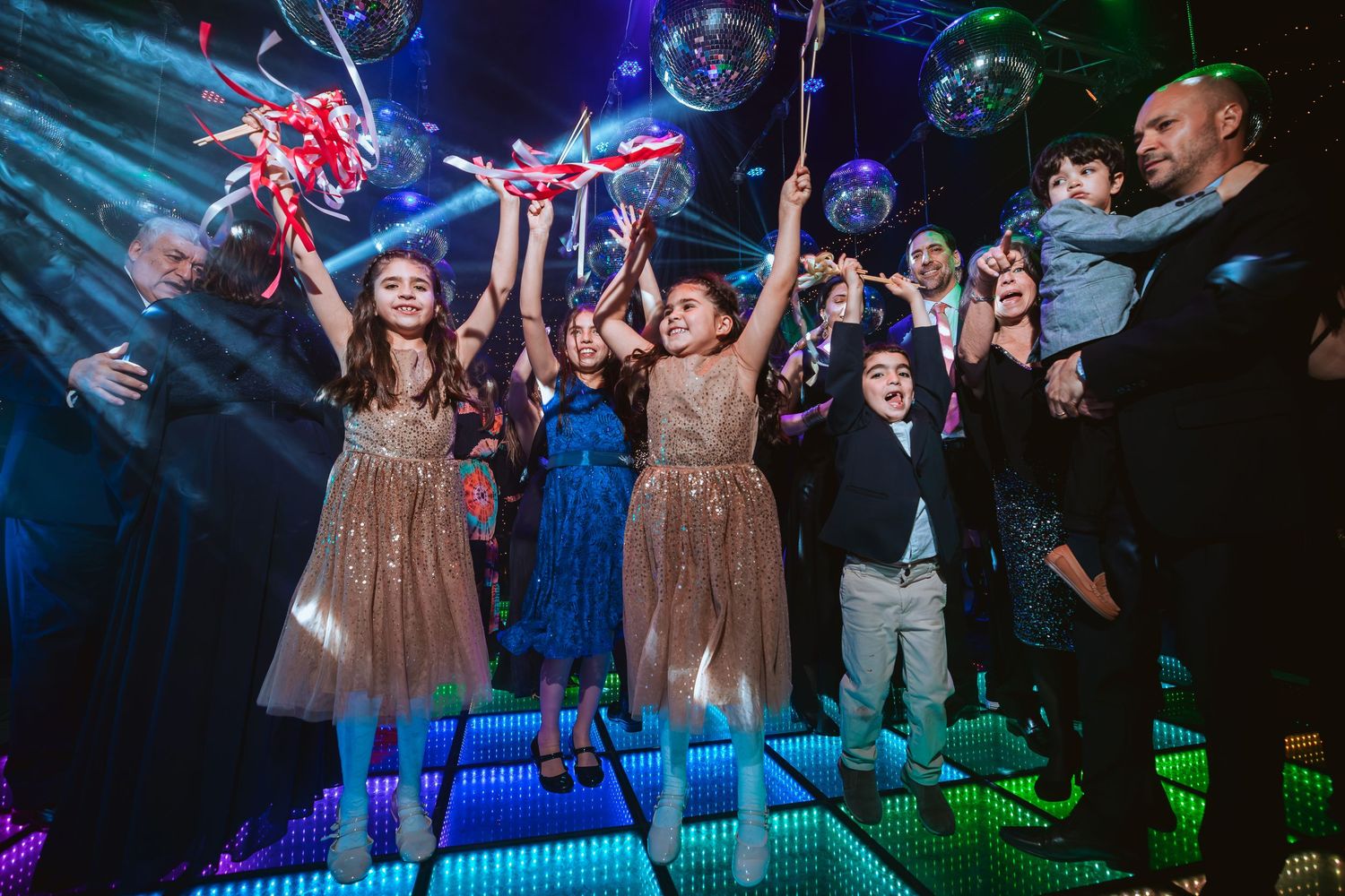 Children in formal attire celebrate at a disco party with mirror balls and colorful laser lights.