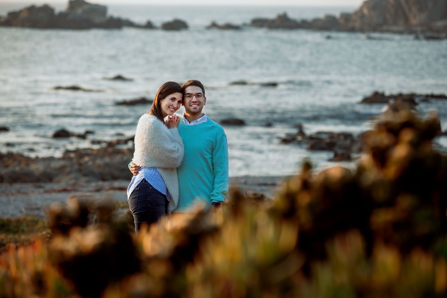 Happy couple embracing near a rocky ocean shore at golden hour.