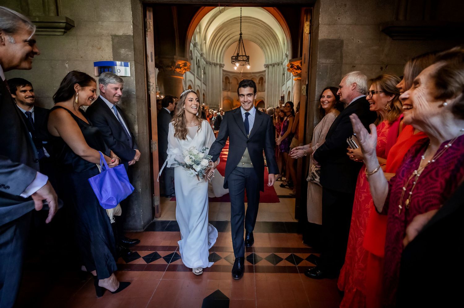 Newlywed couple walks through church corridor as guests celebrate their marriage.