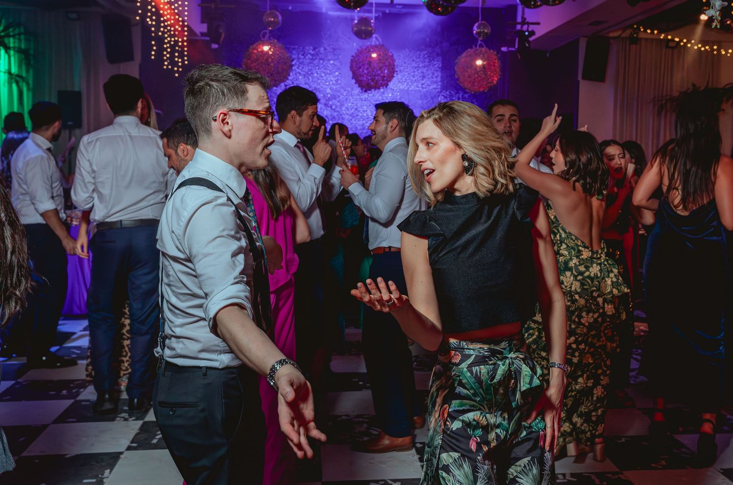 Couple dances together on checkered dance floor at lively wedding reception party.