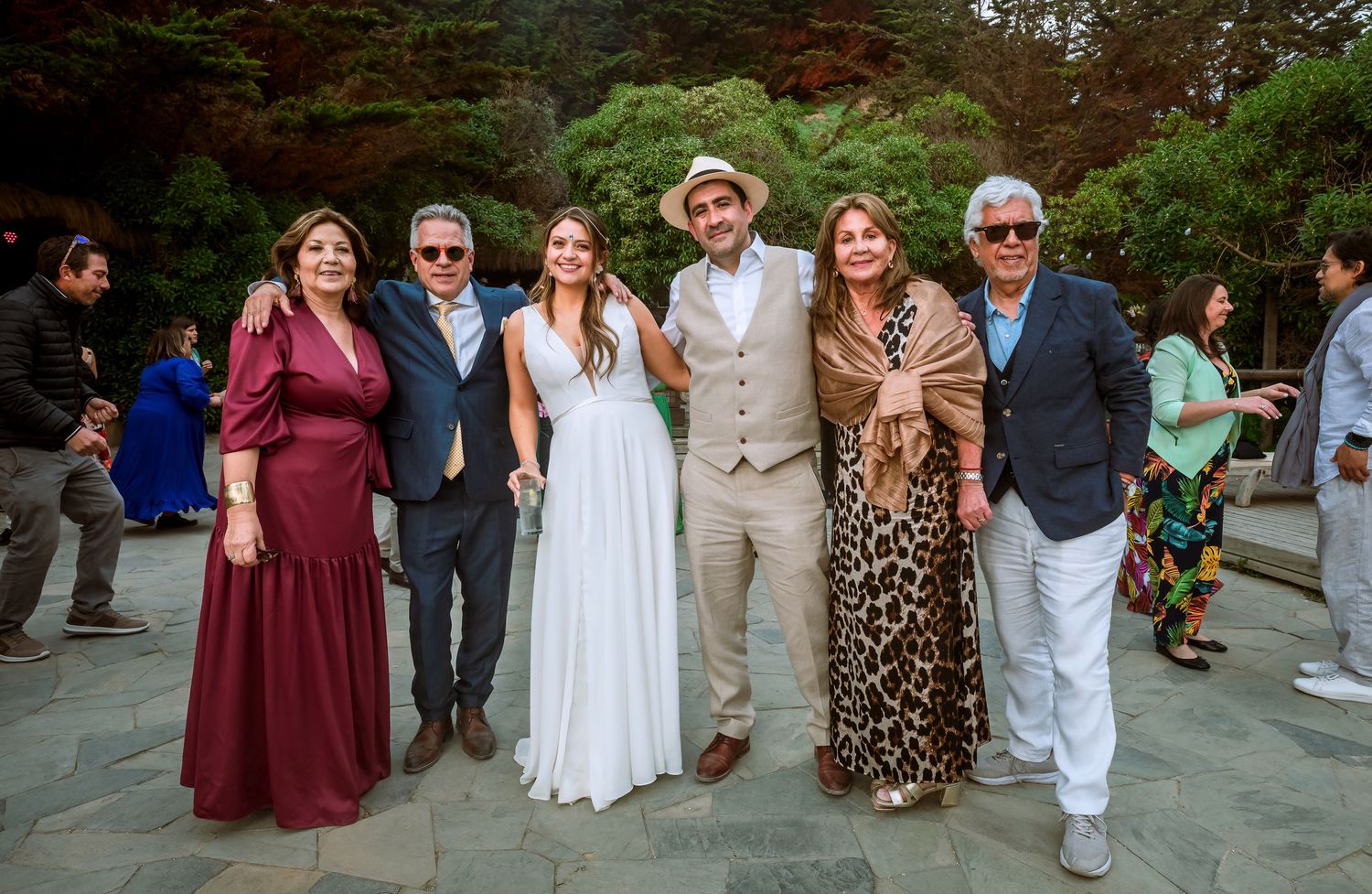 Wedding couple posing with four family members in elegant attire at garden reception.