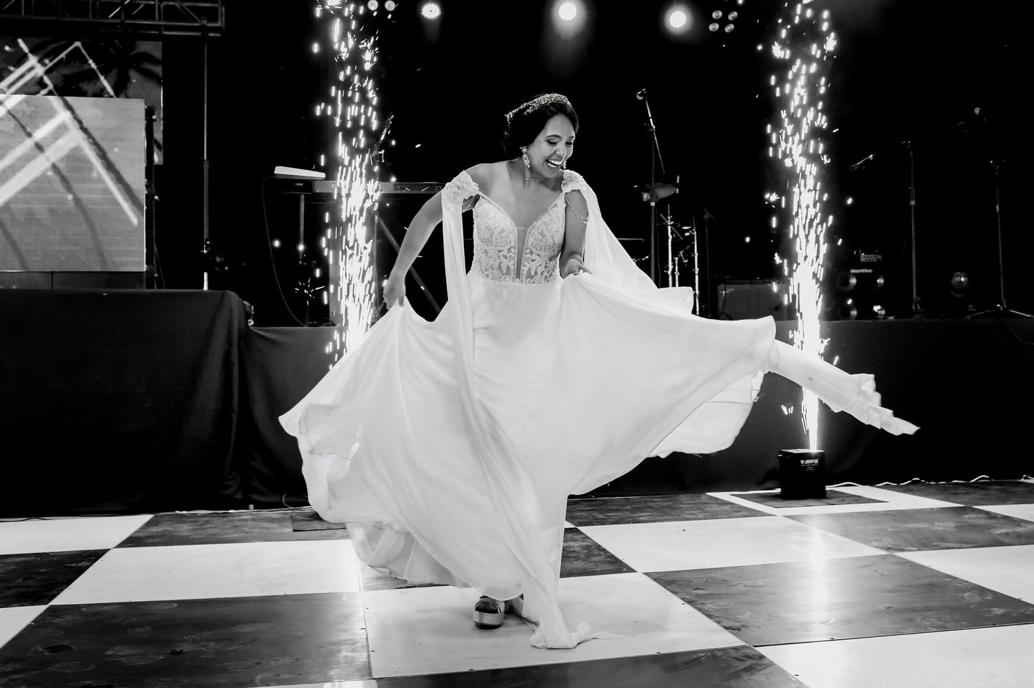 Bride twirling gracefully in flowing white gown on checkered dance floor with sparkling fireworks.