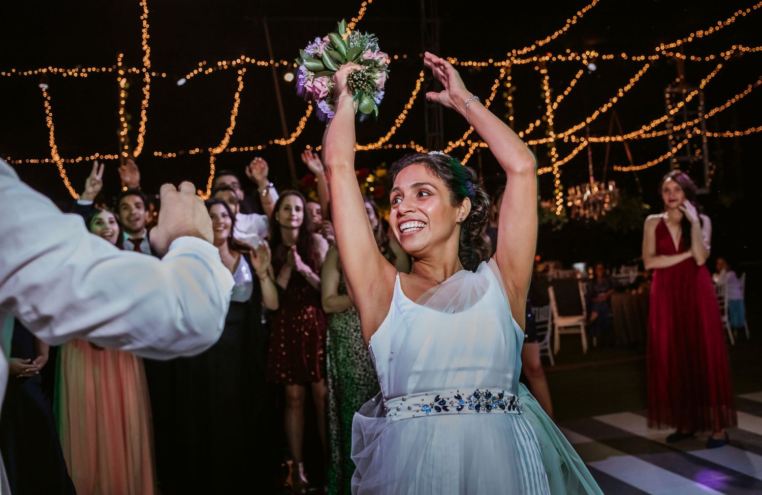 Smiling bride raises bouquet triumphantly before the traditional bouquet toss at wedding.