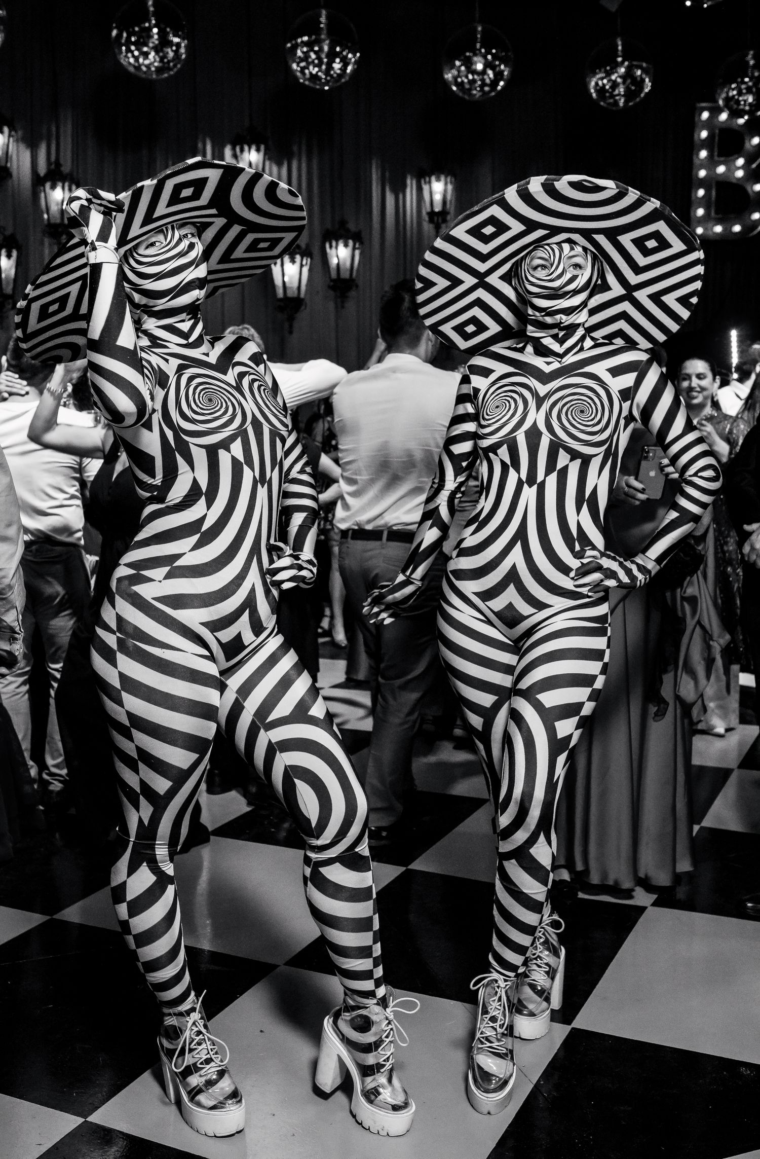 Two performers in striking black and white optical illusion bodysuits and hats pose at an elegant wedding reception.