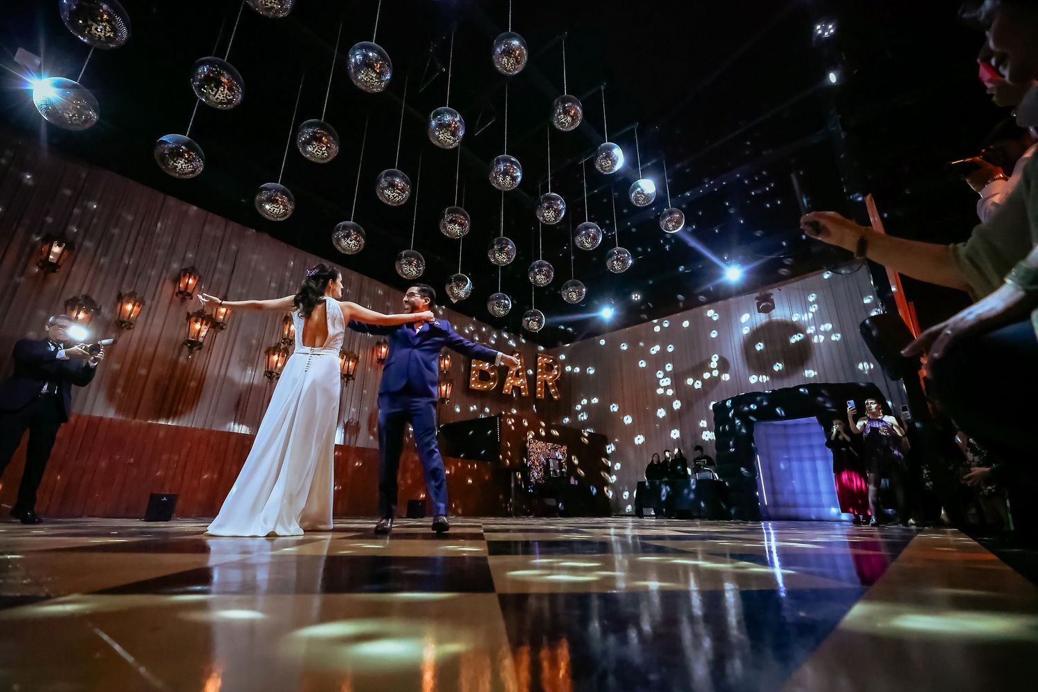 Bride and groom share first dance under glittering hanging disco ball lights on elegant dance floor.