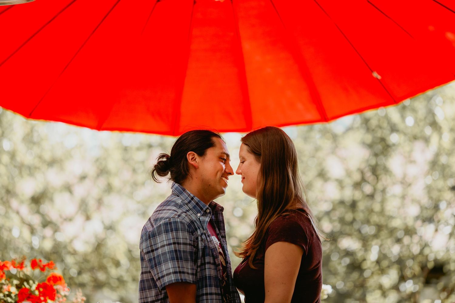 Romantic couple facing each other under a large red umbrella surrounded by soft bokeh lighting.