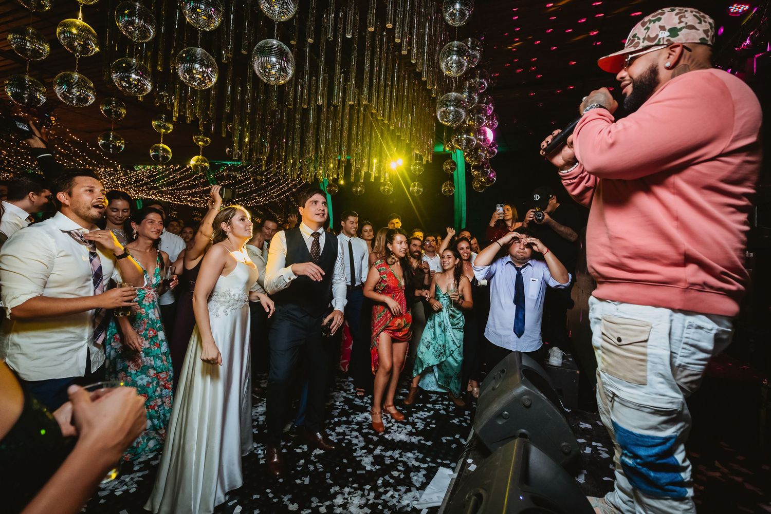 A lively wedding reception with bride and groom on the dance floor as a performer in a pink hoodie entertains guests.