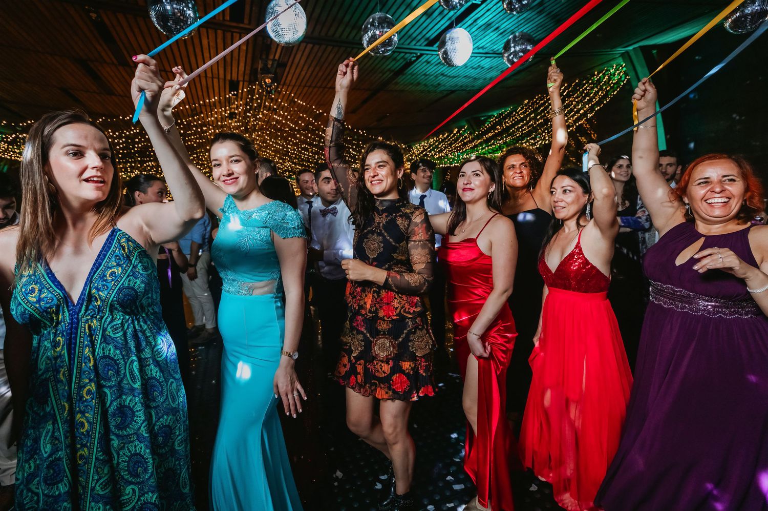 Wedding guests in formal gowns dancing joyfully on confetti-filled dance floor.